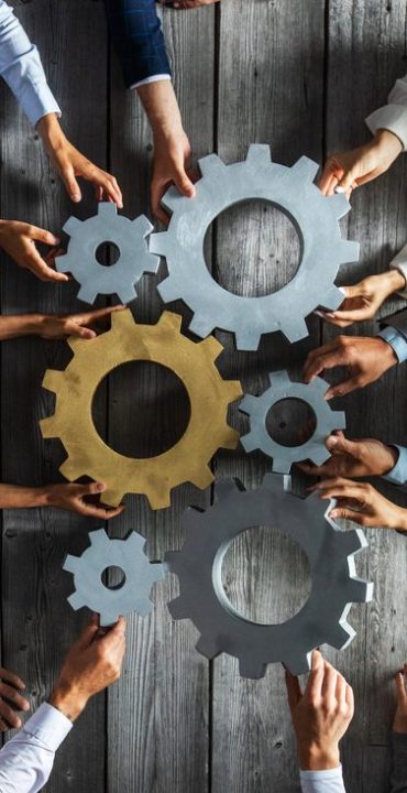 Group of business people joining together silver and golden colored gears on table at workplace top view